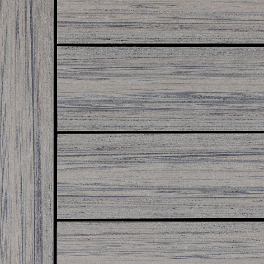 Close-up swatch of Deckorators Voyage Tundra composite decking boards with a matching border board on the left. The boards display a light gray color with soft grain patterns that create a modern wood appearance. The lighter tone helps reflect sunlight and works well for deck surfaces exposed to full sun.