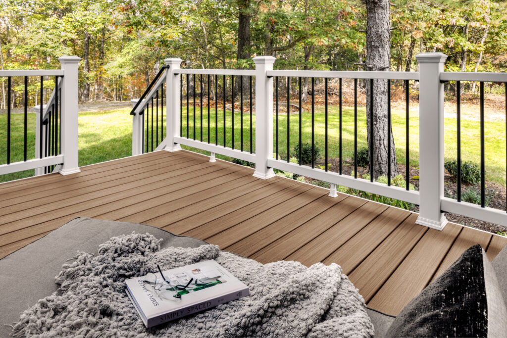 Composite deck with warm brown decking boards and white railing overlooking a wooded backyard. This outdoor space shows how composite decking creates a durable and comfortable deck surface for outdoor living areas exposed to sunlight.