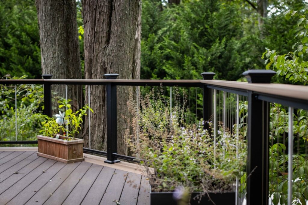 KeyLink Chesapeake vertical cable railing installed on a composite deck surrounded by trees, featuring sleek posts and natural landscaping.