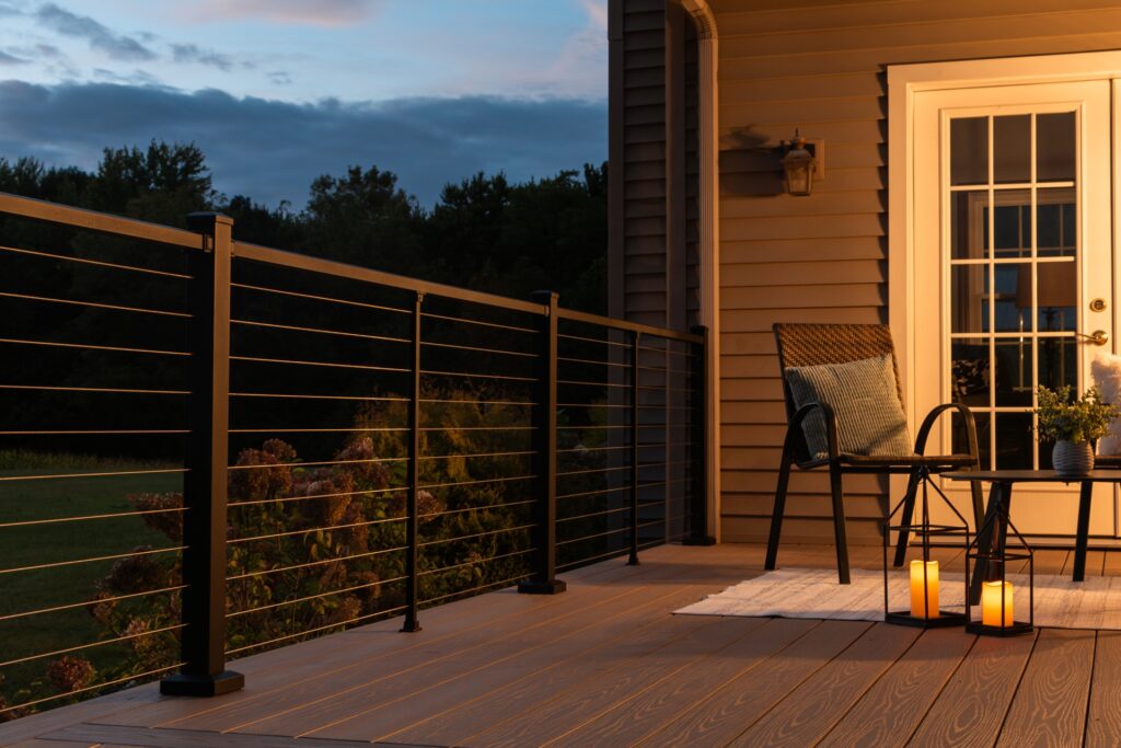Westbury Bella Cavo cable deck railing with horizontal stainless cables installed on a backyard deck at dusk, featuring warm lighting and a modern outdoor seating setup.