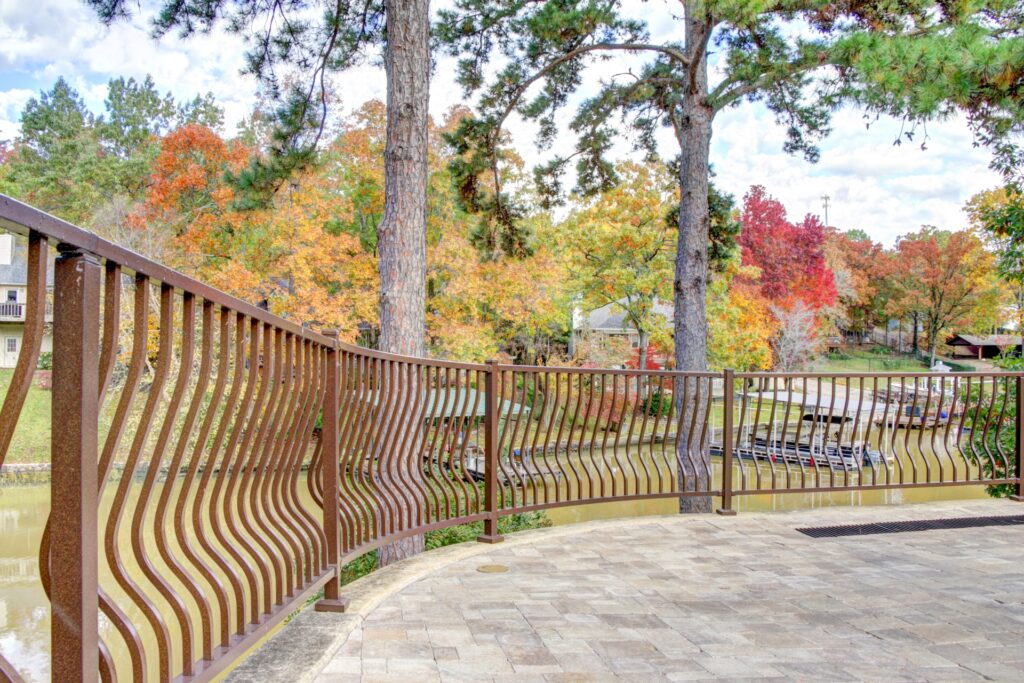 Westbury Montego aluminum railing with curved decorative balusters installed along a stone patio overlooking a wooded lakeside setting with fall foliage.