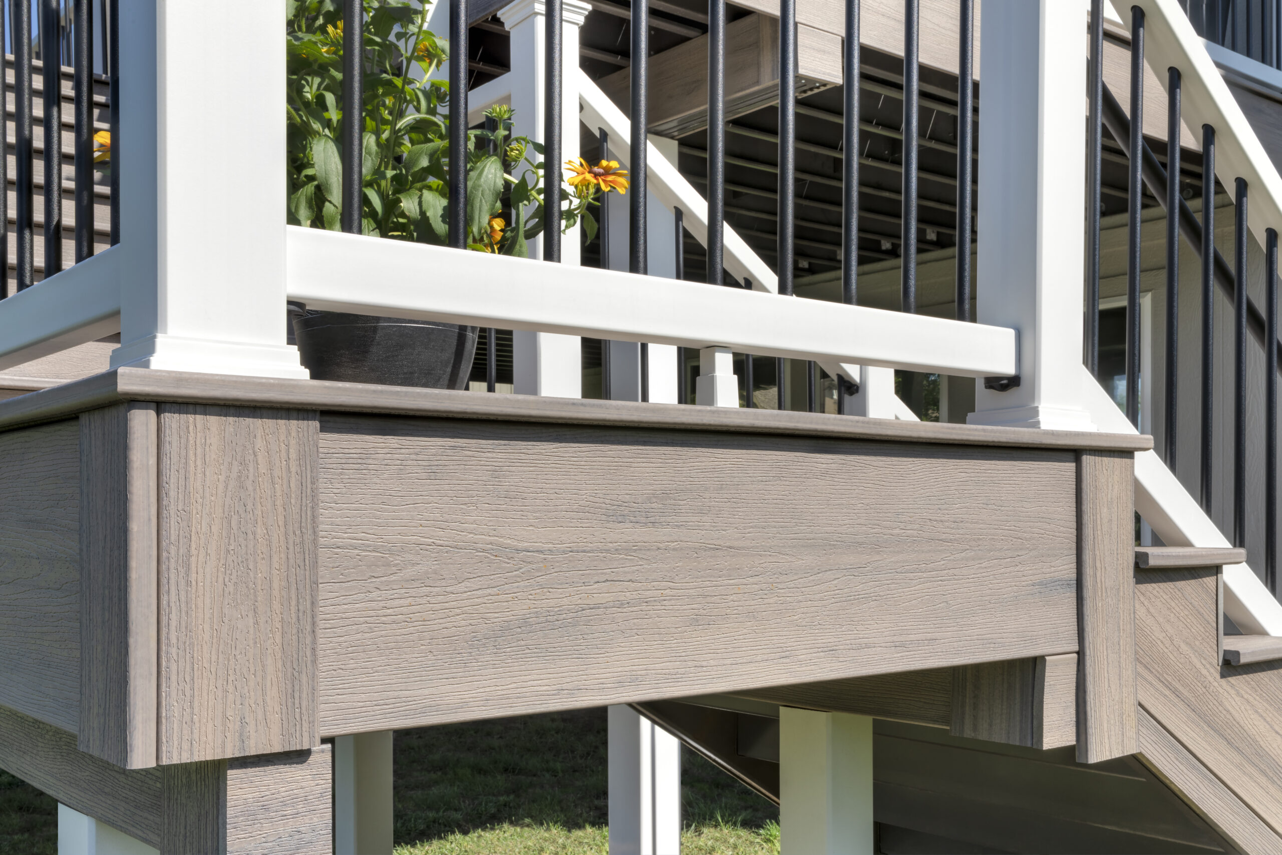 What is a fascia board - close-up of gray composite fascia board installed flush below the deck surface at a corner post, showing wood-grain texture and clean edge finish