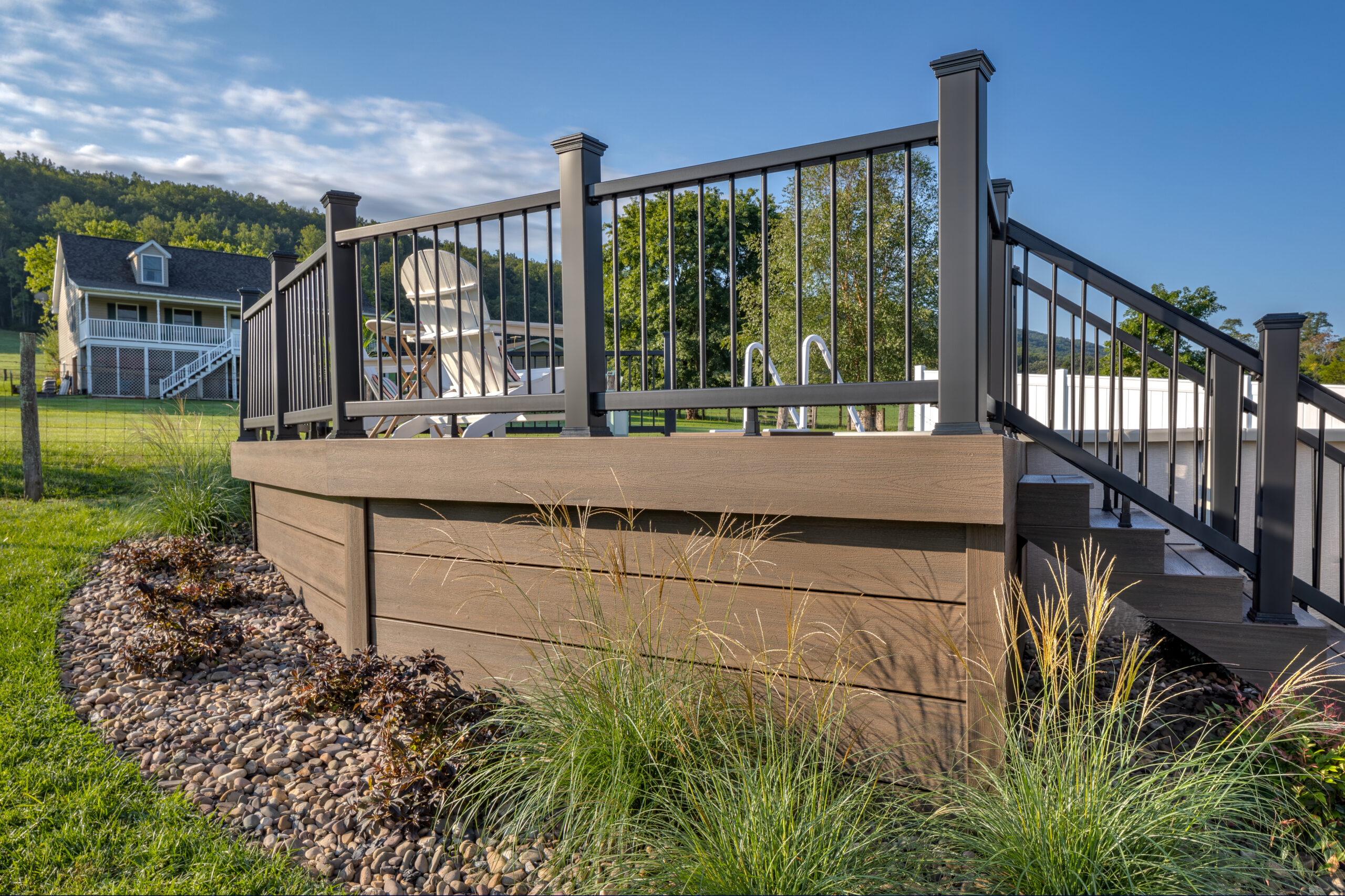What is a fascia board on a deck - full view of brown composite fascia boards wrapping the entire perimeter of a raised backyard deck surrounded by ornamental grasses and landscaping

