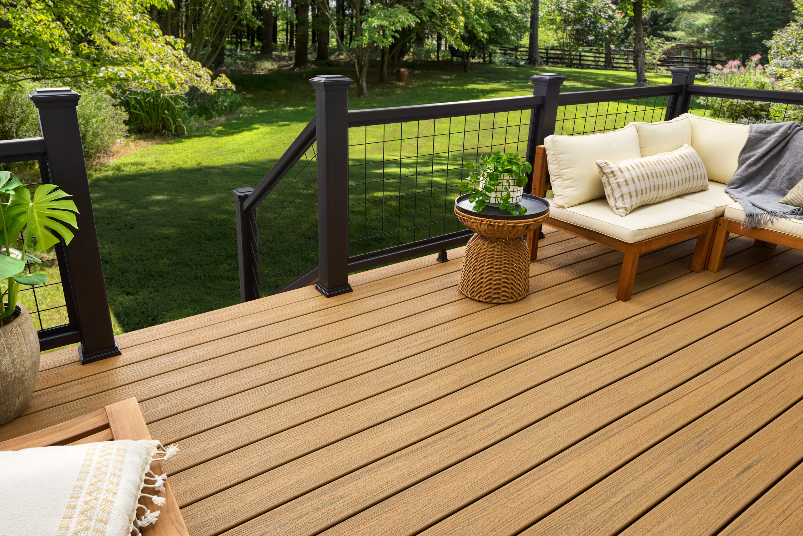 Raised composite deck with cushioned seating, wicker side table, and black grid railings surrounded by trees