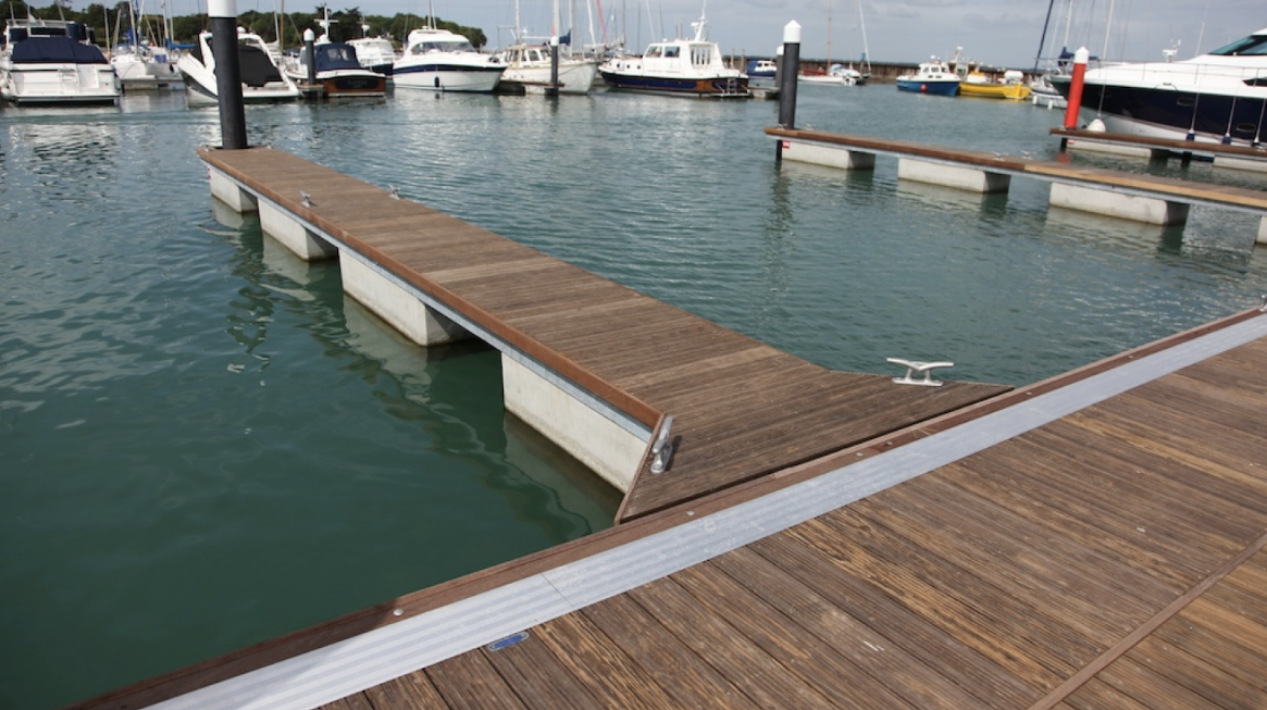 Aerial view of a private boat dock with piling construction and Adirondack chairs attached to a luxury waterfront home