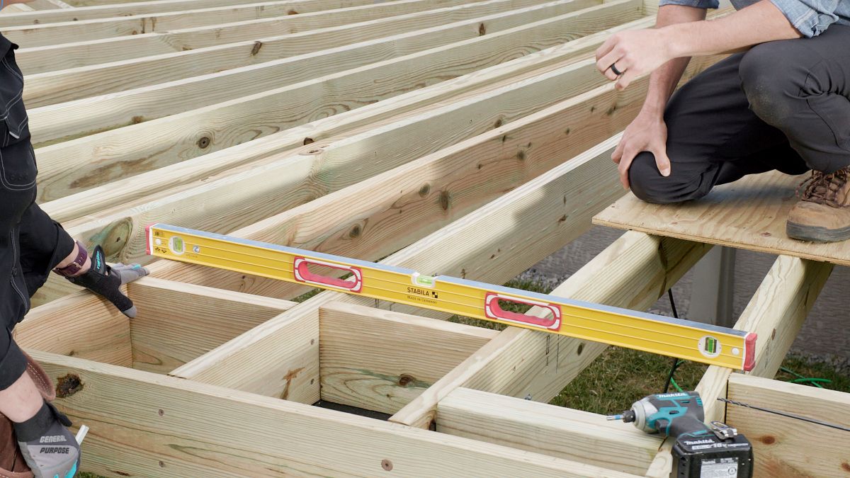 Deck builders leveling pressure treated joists during framing under 2024 IRC guidelines