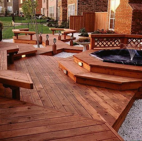 Multi-level redwood deck with built-in benches hot tub and landscape lighting in a residential backyard