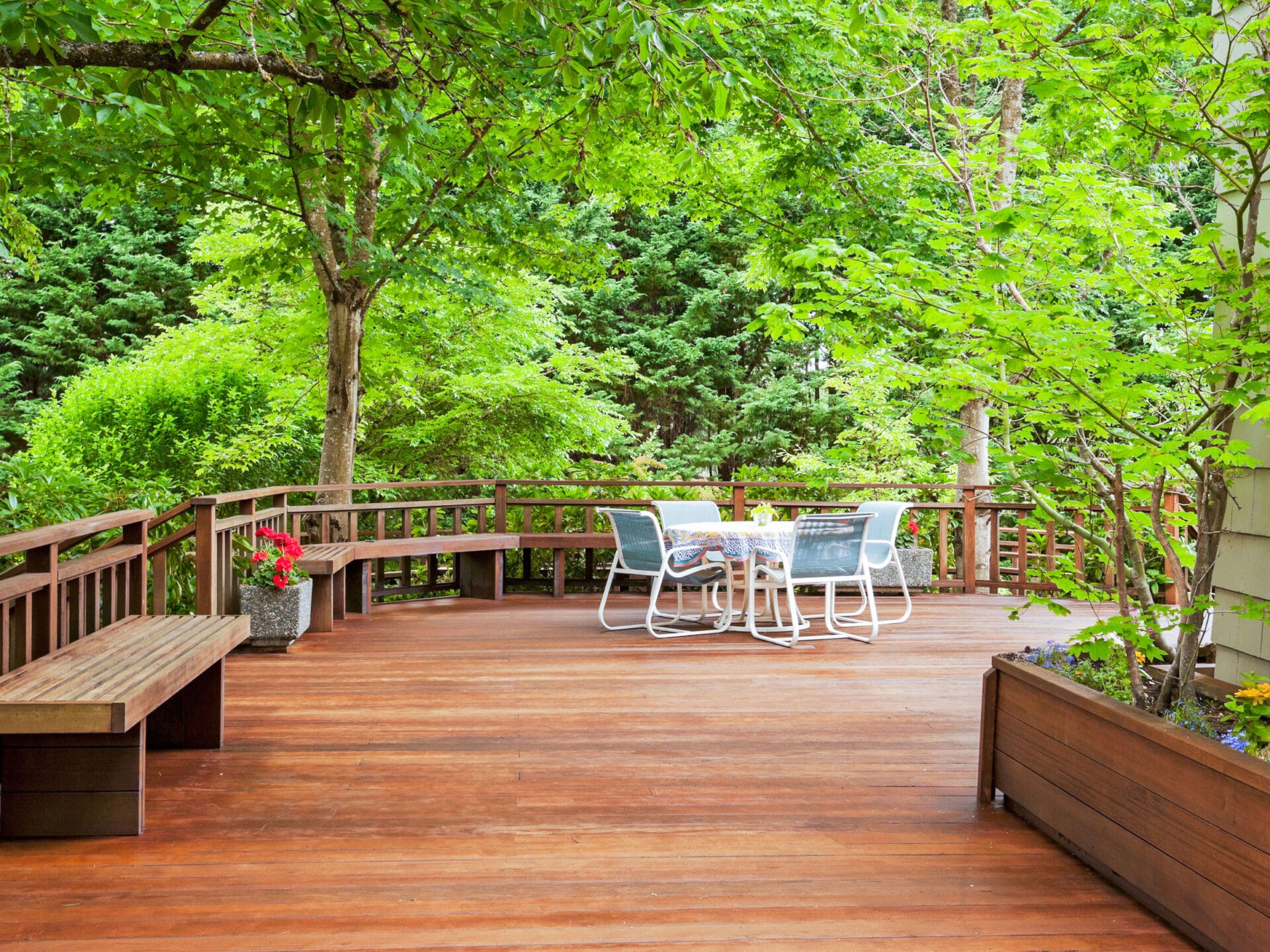 Wide wood deck with log cabin railing showing warm reddish-brown decking boards overlooking a forested lake view