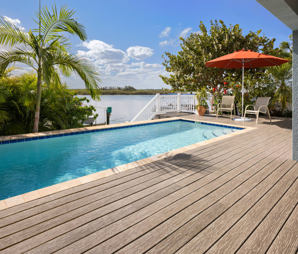 MoistureShield Vision Mochaccino composite deck surrounding pool with palm trees and umbrella seating