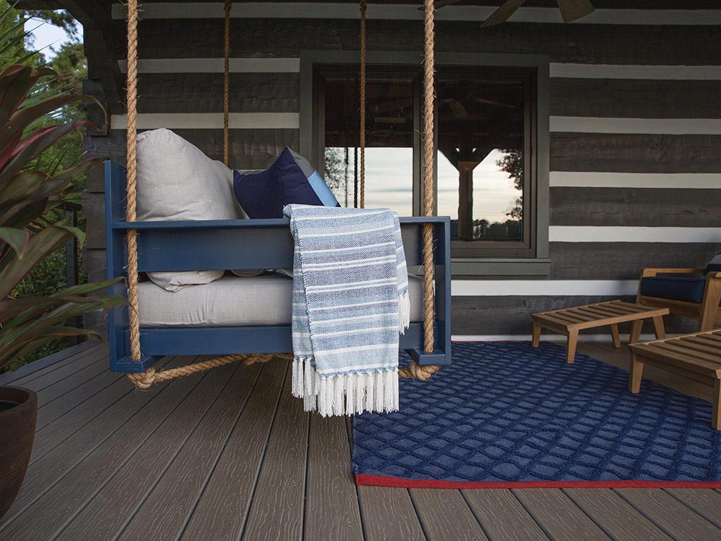 MoistureShield Vision Smokey Gray composite deck porch with hanging swing bed and log cabin