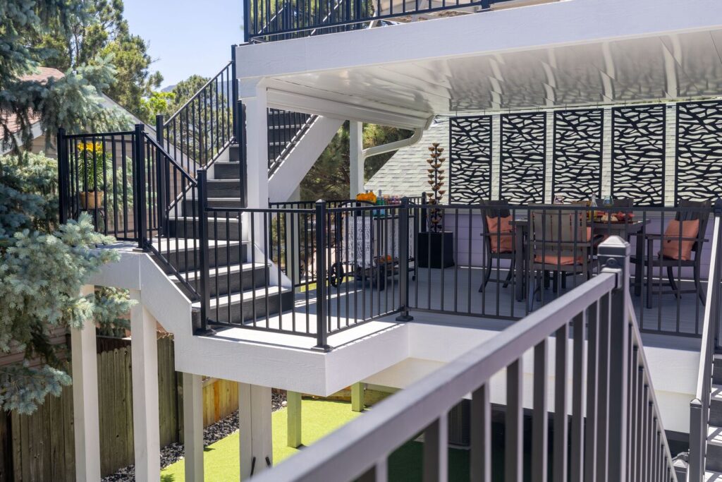 Black Envision Fairway modern steel railing on a two-level deck with switchback stairs, white fascia and laser-cut privacy screens, metal deck railing ideas for multi-level decks.