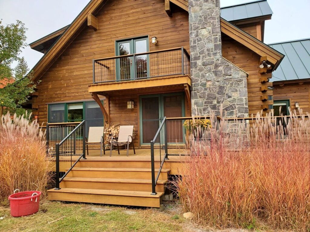 Fortress Cable V-Series vertical steel cable railing with wood top rail on a log cabin deck
