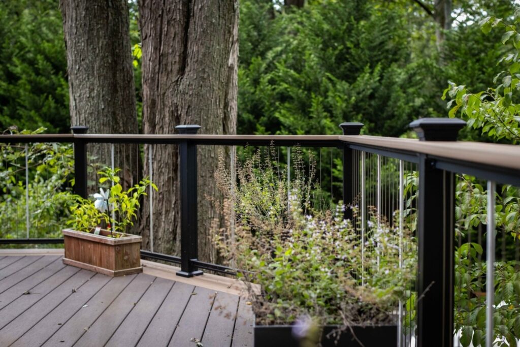 KeyLink Chesapeake vertical cable railing with a composite top rail against tall trees, open metal deck railing ideas.