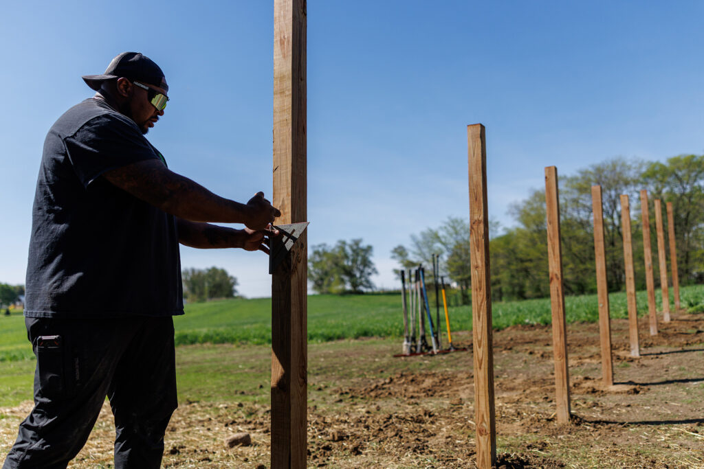 Installer marking a treated fence post with a speed square along a run of set ProWood posts.