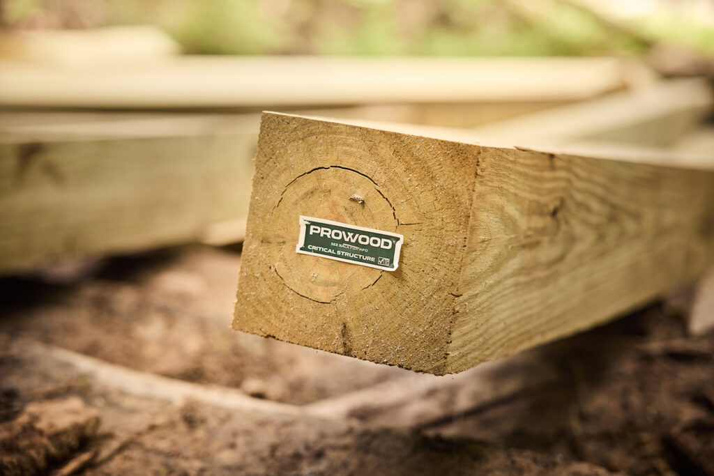 ProWood Critical Structure end tag stapled to the cut end of a treated post resting on soil.