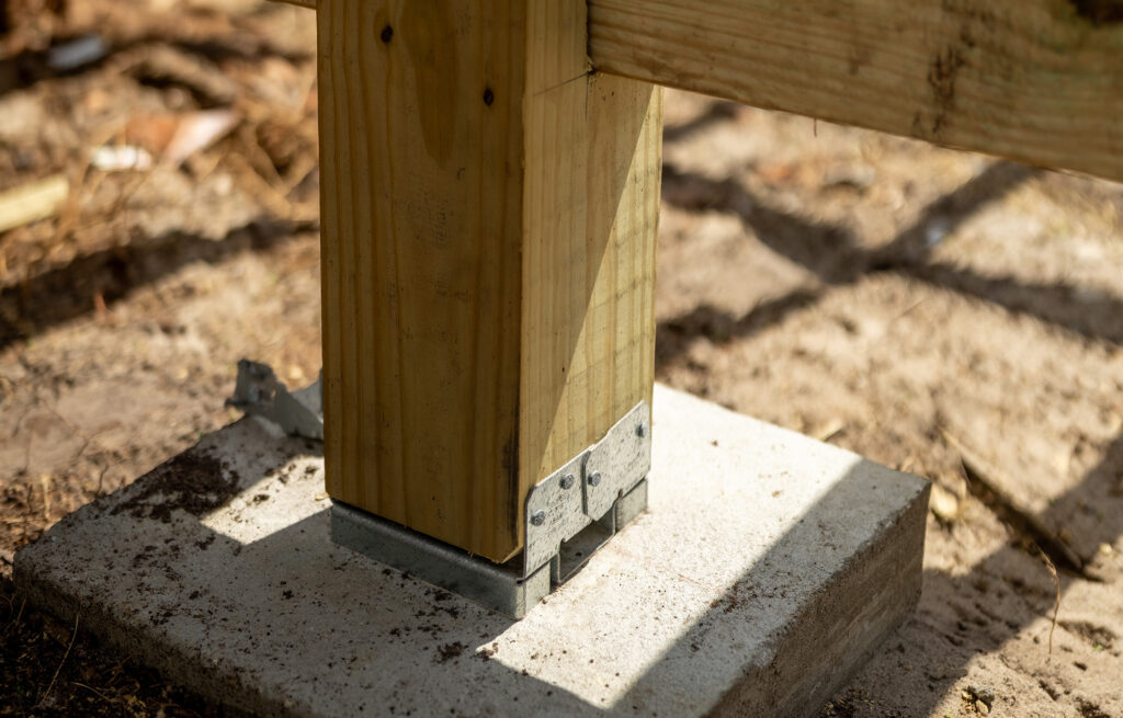 ProWood treated deck post on a galvanized standoff base, raised off the concrete footing to shed water.