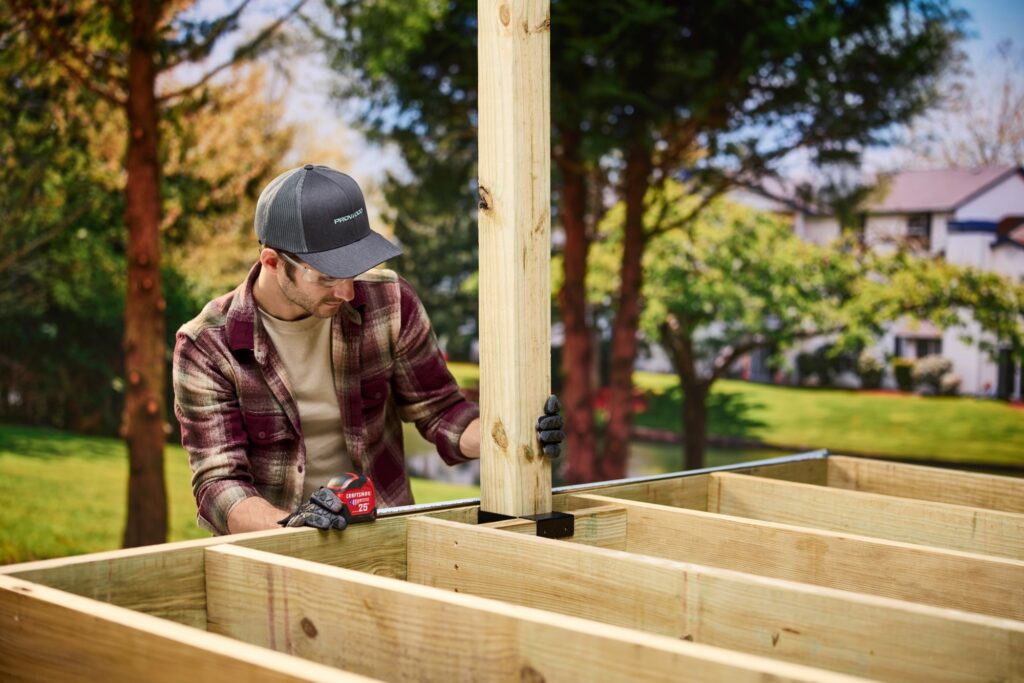 Builder in a ProWood cap plumbing a treated 4x4 deck post seated in a black steel post base.