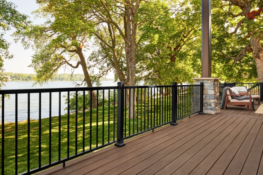 Black TimberTech Fulton Rail on an AZEK English Walnut deck overlooking a lake, with a stone column and covered seating.