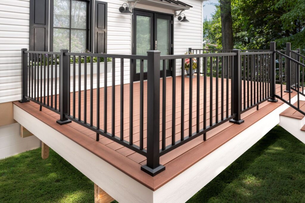 Black Trex Select aluminum railing with square balusters on a warm redwood-toned composite deck at a white farmhouse.