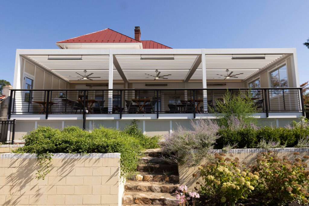 Black Trex Signature Rod Rail running along a covered wine bar terrace under a louvered pergola.