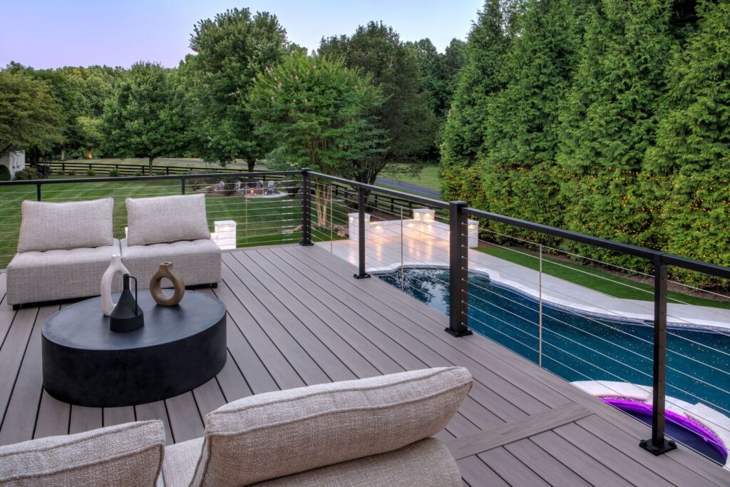 Trex Signature X-Series cable railing around an elevated composite deck overlooking a lit pool at dusk, modern metal deck railing ideas.