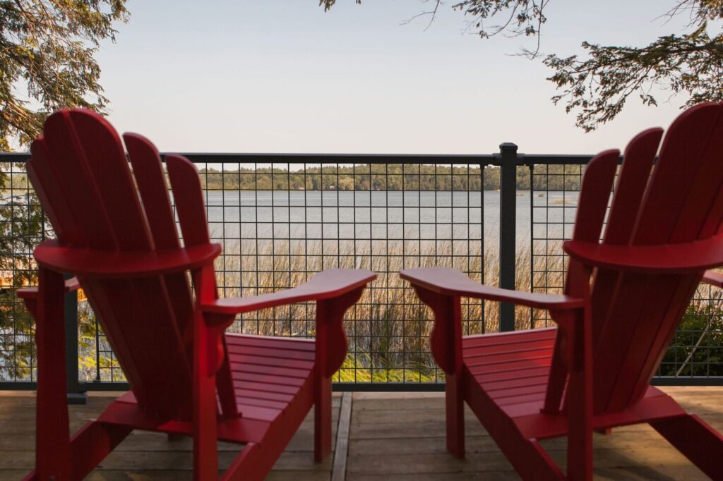 Black Westbury mesh panel railing framing a lake view behind two red Adirondack chairs.