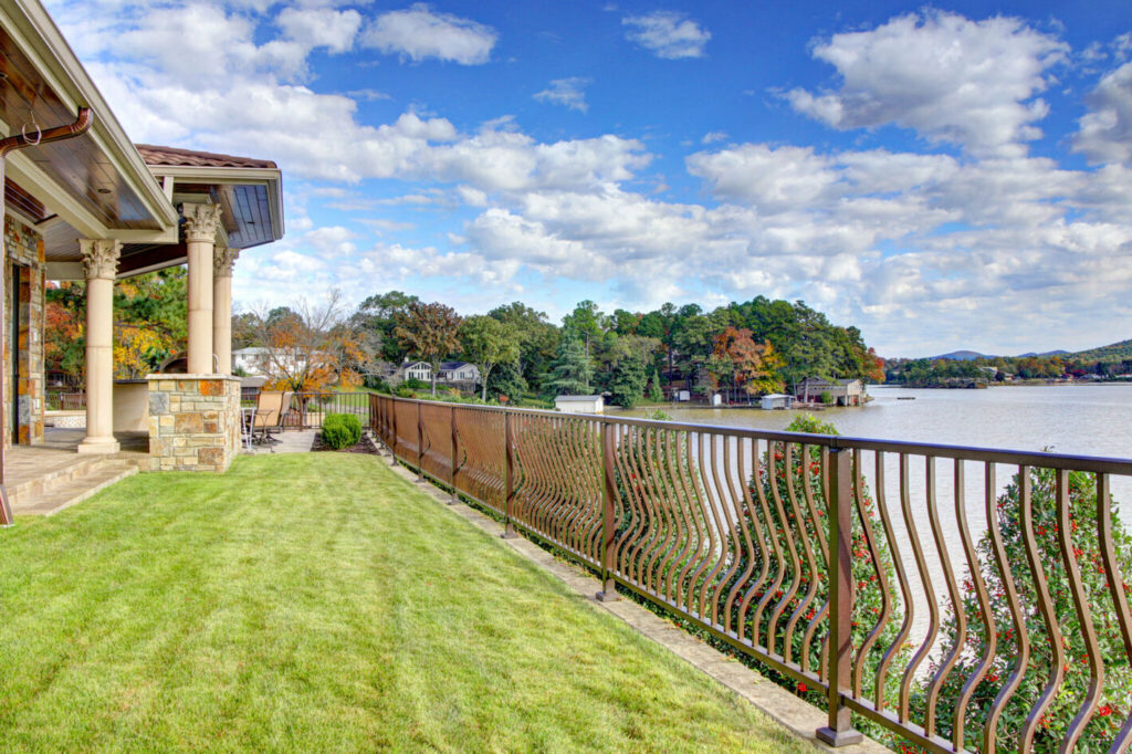 Westbury Montego bronze aluminum railing with curved balusters along a lakefront lawn.