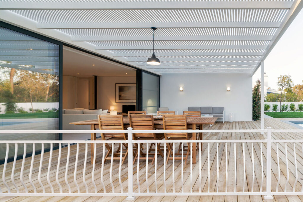 Textured white Westbury Montego aluminum railing with curved balusters on a light wood deck under a louvered pergola, white metal deck railing ideas.