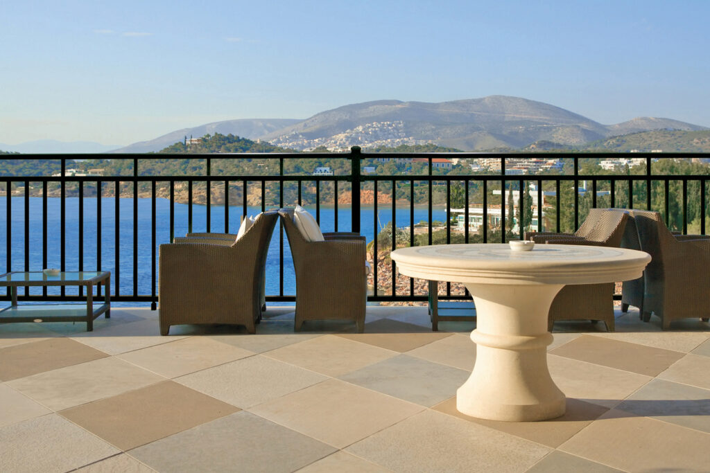 Black Westbury Riviera aluminum railing along a stone-tiled seaside terrace overlooking a bay and mountains.