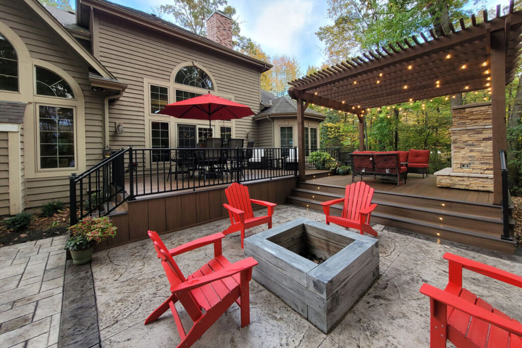 Black Westbury Tuscany aluminum railing on a multi-level deck with lit stair risers, a pergola and a fire pit patio.