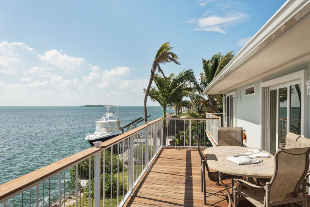 White Westbury VertiCable railing with a wood drink rail cap on a narrow oceanfront balcony in the Florida Keys.