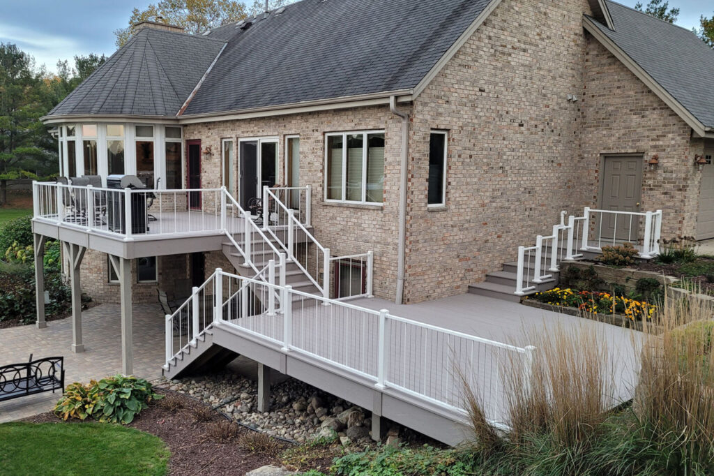 Textured white Westbury VertiCable railing with vertical stainless cable on a multi-level gray composite deck at a brick home.