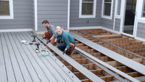 Composite deck boards being installed over a wood deck frame by a homeowner who used a deck materials list