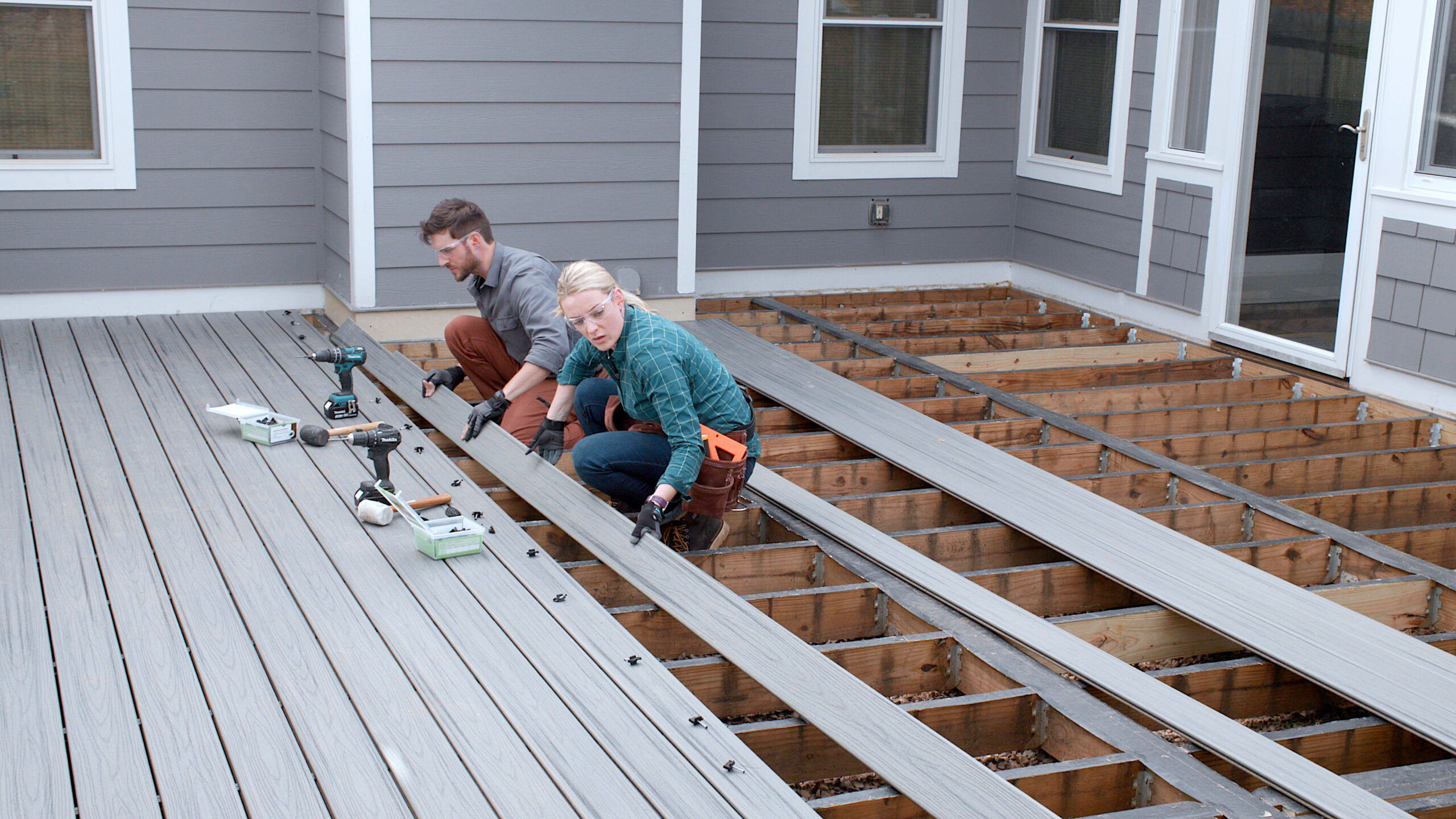 Composite deck boards being installed over a wood deck frame by a homeowner who used a deck materials list