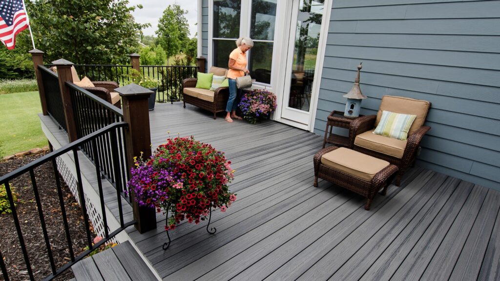 Envision Distinction Grey Wood deck with black baluster railing, wicker seating, and colorful flower planters.