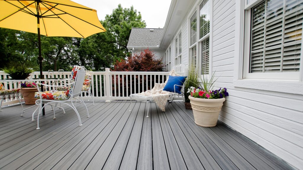 Envision Distinction Grey Wood deck with white railing, yellow patio umbrella, outdoor furniture, and flower planters.