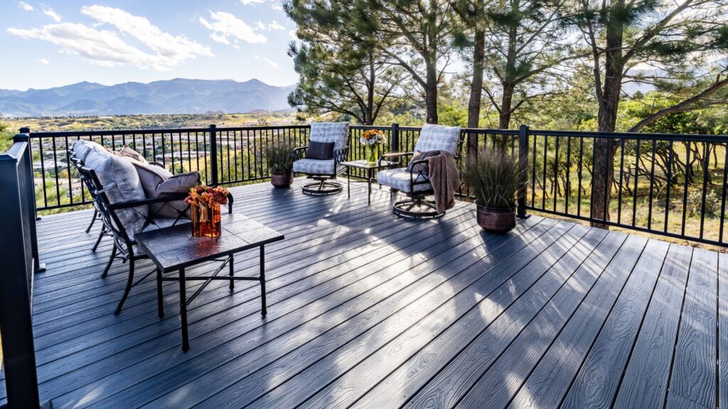 Envision deck ideas featuring Distinction Grey Wood decking with black railing, outdoor seating, pine trees, and mountain views.