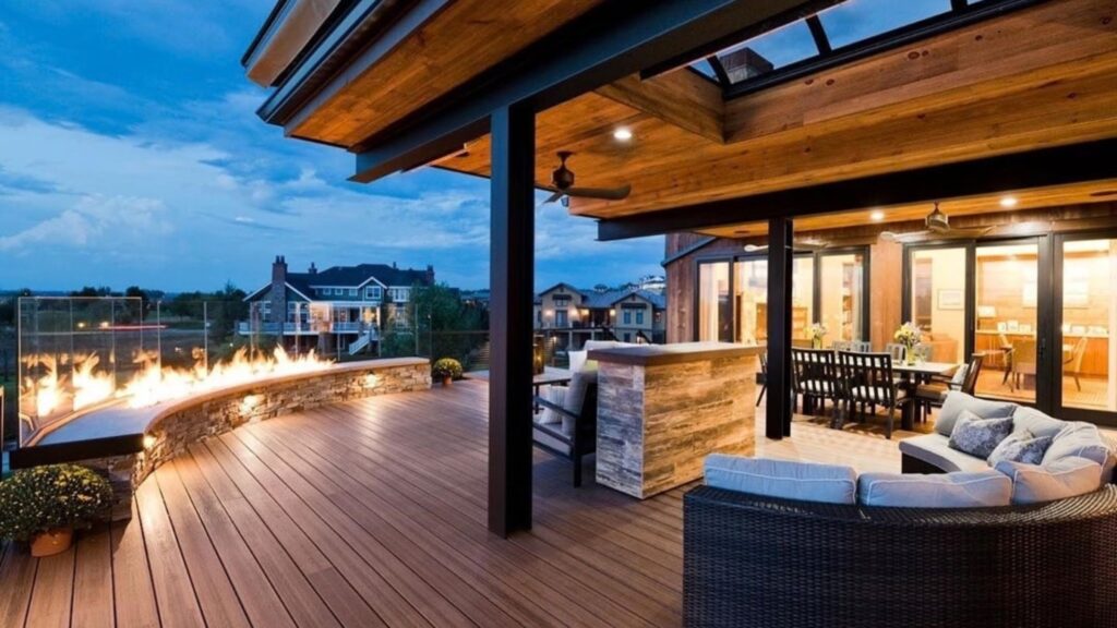 Envision Distinction Spiced Teak covered deck with curved fire feature, outdoor bar, dining area, lounge seating, and lighting.