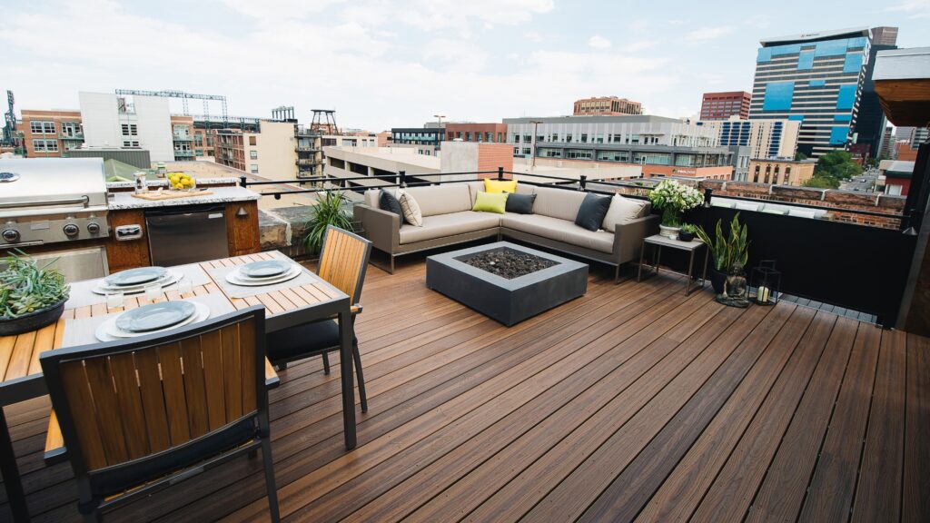 Envision Distinction Spiced Teak rooftop deck with outdoor kitchen, dining area, sectional seating, fire feature, and city views.