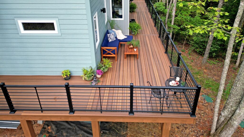 Envision Distinction Spiced Teak deck with black horizontal railing, lounge seating, planters, and wooded surroundings.