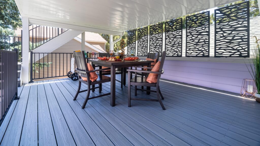 Envision Ridge Premium Alpine Fog covered deck with outdoor dining furniture, black railing, and decorative privacy screen panels.