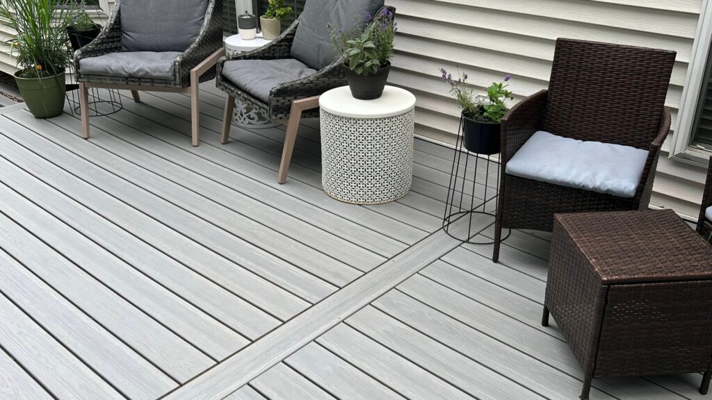 Envision deck ideas featuring Ridge Premium Alpine Fog decking with wicker chairs, small accent tables, potted plants, and light siding.