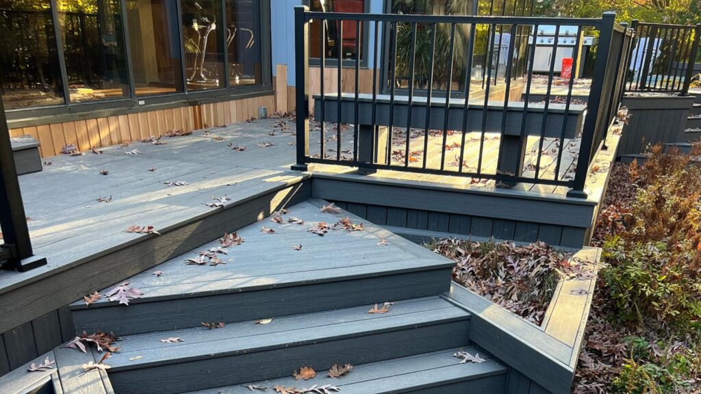 Fiberon Sanctuary Earl Grey deck with angular gray stairs, black railing, dark fascia, and bordered planting area.
